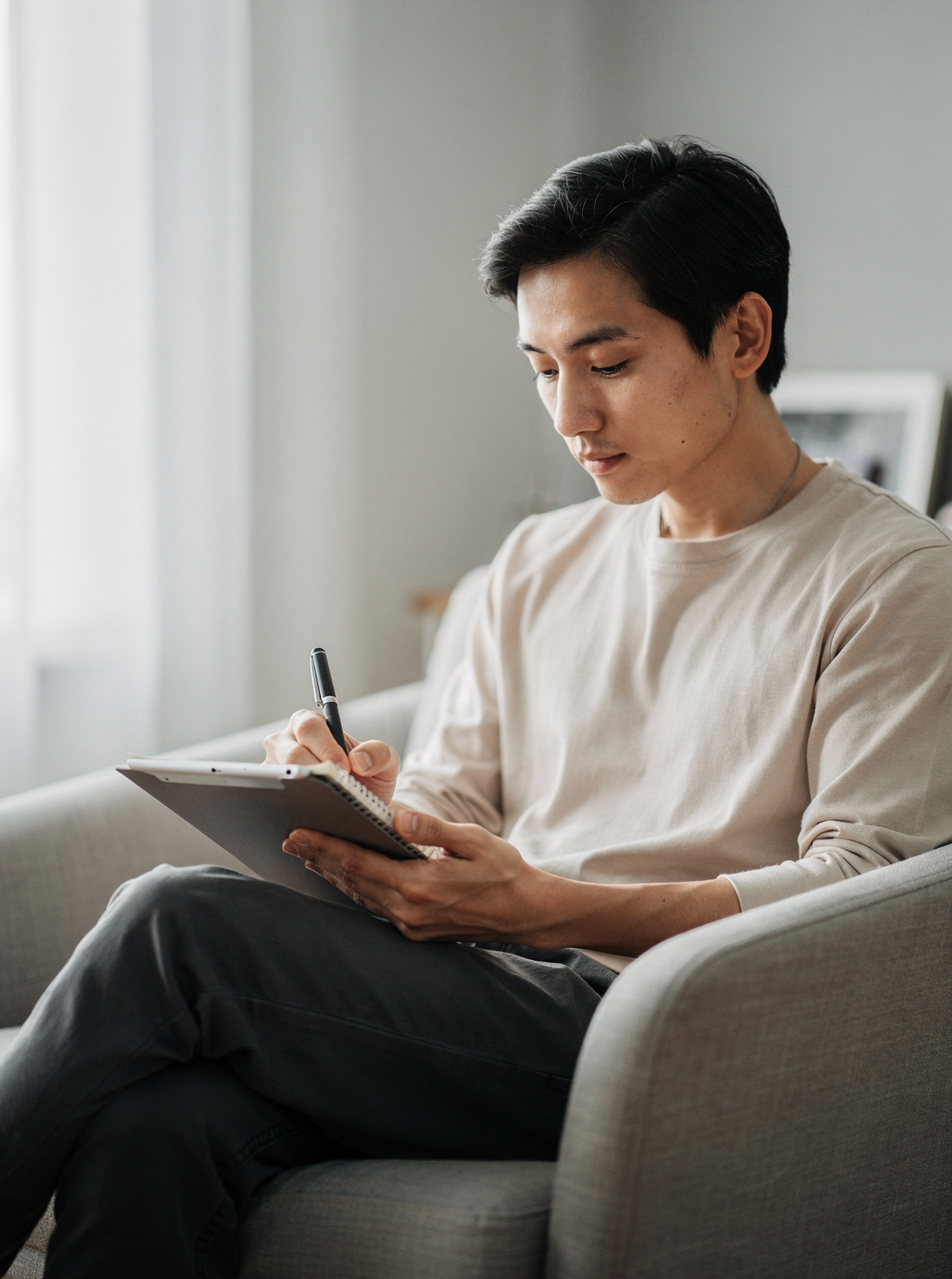 A man sits in an armchair and writes in a notebook.